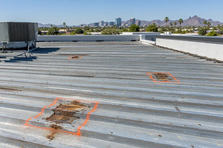 Exposed corrugated metal roof deck during a commercial reroof, a few rusted spots marked for replacement