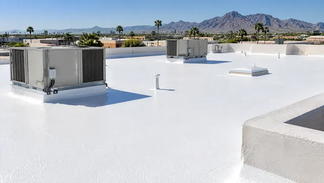 Freshly coated spray polyurethane foam roof on a flat commercial building in Phoenix, bright white elastomeric coating with a slightly textured orange-peel surface, HVAC units and parapets