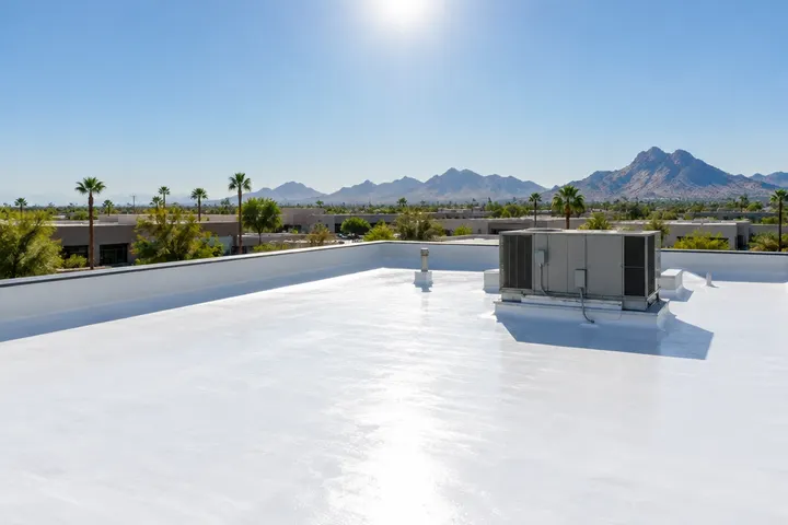 Bright white reflective coated flat roof under intense desert midday sun, heat shimmer in the air, parapet and HVAC unit